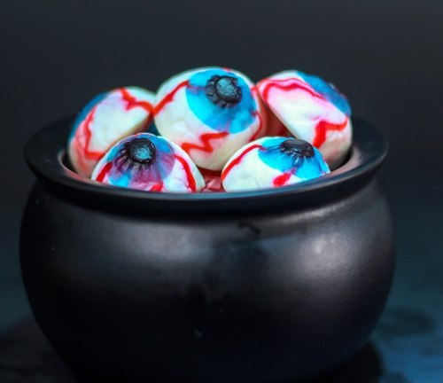 A black cauldron filled with colorful, spooky eyeball treats with blue and red designs.