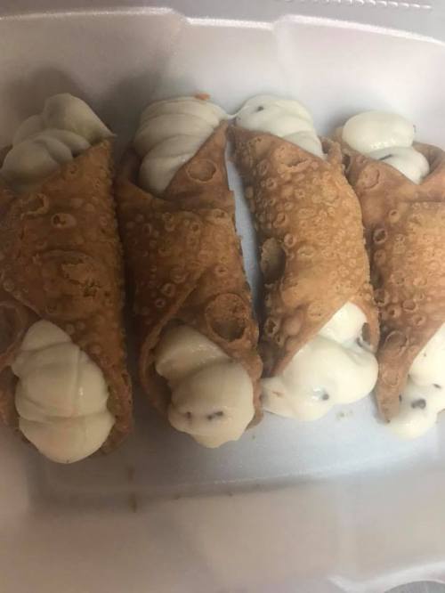 Four crispy cannoli filled with creamy ricotta and chocolate chips, arranged neatly in a takeout container.