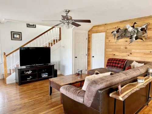 Cozy living room with a brown sofa, wooden accents, a TV, and a staircase in a bright, inviting space.