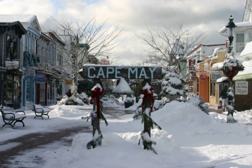 Snow-covered street in Cape May, adorned with holiday decorations and a sign welcoming visitors.