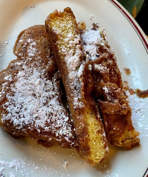 Two pieces of French toast dusted with powdered sugar on a white plate.