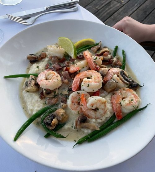 A plate of shrimp and mushrooms on a bed of creamy grits, garnished with green beans and lime slices.
