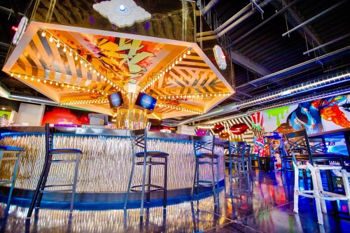 A vibrant bar with a unique ceiling design, colorful murals, and stylish seating in a lively atmosphere.