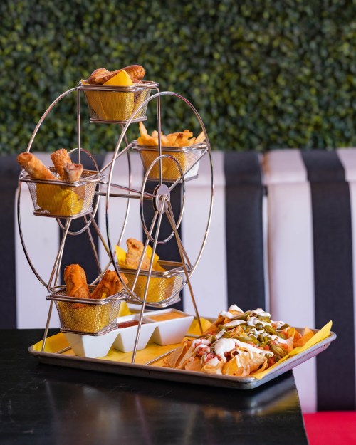 A creative food display featuring a ferris wheel with chicken wings and nachos on a tray, set against a green backdrop.