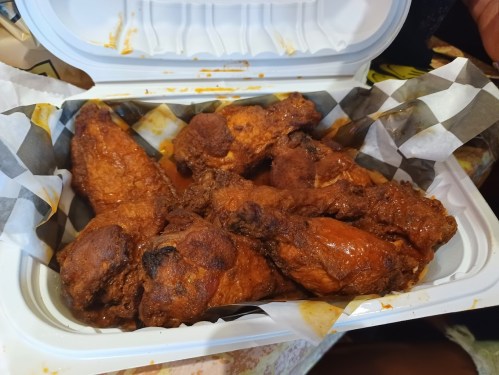 A takeout container filled with crispy, sauced chicken wings on a checkered paper lining.