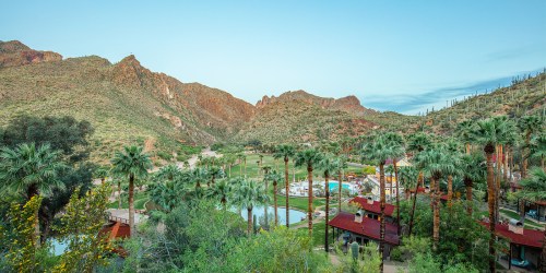 A scenic view of a resort surrounded by palm trees and mountains under a clear blue sky.