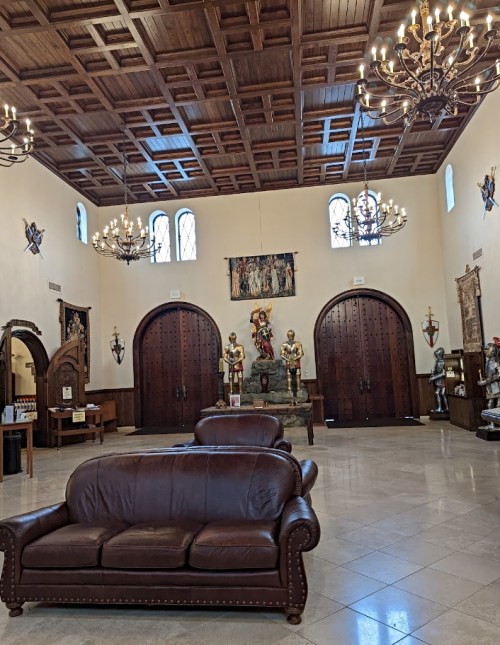 A spacious room with a leather sofa, wooden doors, chandeliers, and decorative statues.