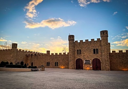 A stone castle with towers under a colorful sunset sky, featuring large wooden doors and a paved courtyard.