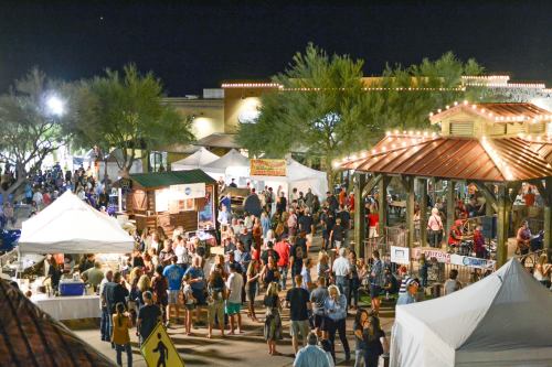A lively night market scene with crowds, food stalls, and festive lights under a clear sky.