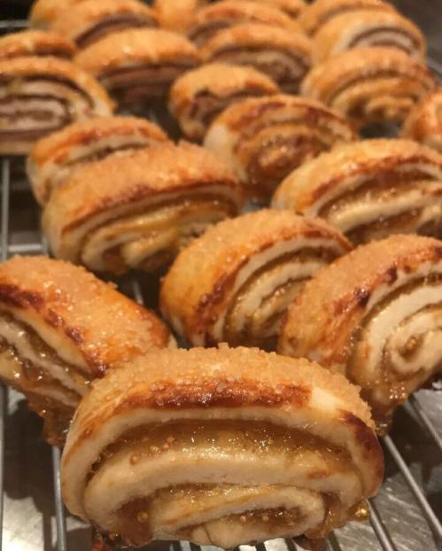 A close-up of golden-brown, flaky pastry rolls with a sugary glaze, arranged neatly on a cooling rack.