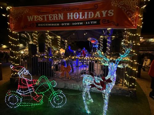 A festive scene with a "Western Holidays" banner, decorated with lights, featuring a Santa on a motorcycle and a reindeer.