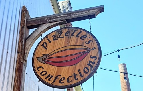 Sign for "Pizzelle's Confections" featuring colorful confections and a clear blue sky in the background.