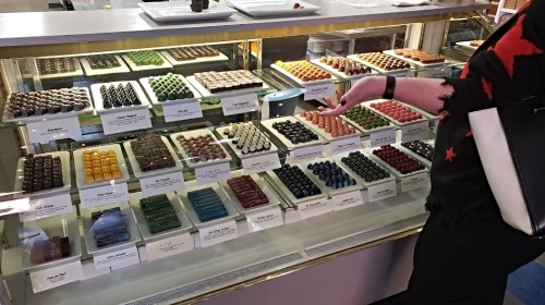 A display case filled with colorful chocolates and confections, with a person gesturing towards the selection.