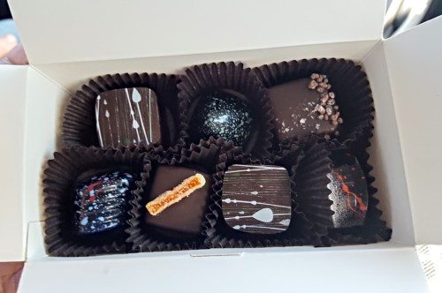 A box of assorted chocolates, featuring various designs and toppings, arranged in black paper liners.