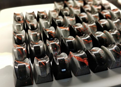 A close-up of glossy, black and orange chocolate bonbons arranged neatly on a white platter.