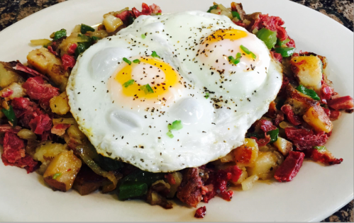 A plate of hash with corned beef, diced potatoes, green peppers, and two sunny-side-up eggs on top, garnished with pepper.