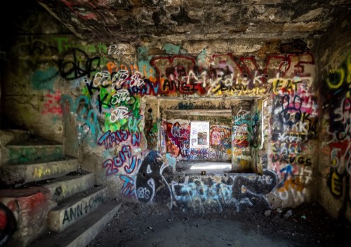 A dimly lit, abandoned room covered in vibrant graffiti and colorful street art on the walls.