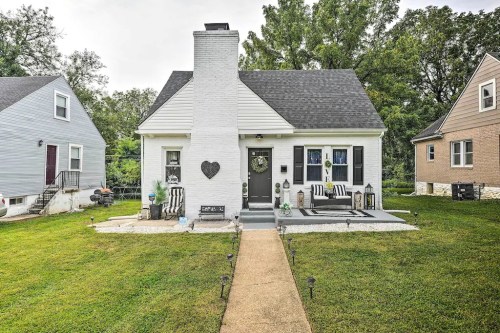 A charming white house with a black roof, surrounded by greenery and a well-kept lawn, featuring a welcoming front porch.
