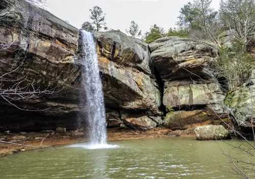 A serene waterfall cascading over rocky cliffs into a calm pool, surrounded by trees and natural greenery.