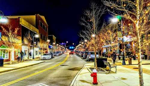 A vibrant street at night, lined with trees adorned with lights, shops, and parked cars, creating a festive atmosphere.