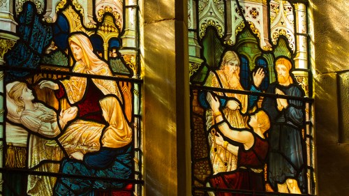 Stained glass window depicting biblical figures in a scene of healing and compassion.