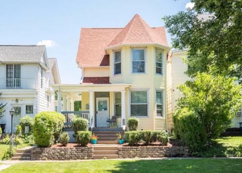 A charming yellow Victorian-style house with a red roof, surrounded by greenery and a well-maintained garden.