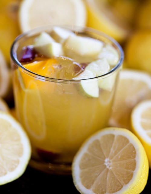 A refreshing glass of citrus drink with lemon and apple slices, surrounded by fresh lemon halves.