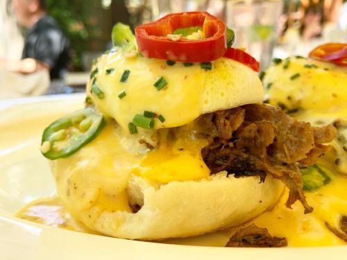 A close-up of a savory dish featuring a soft bun topped with melted cheese, herbs, and sliced peppers.