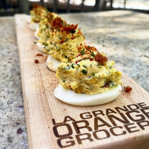 A wooden board displays beautifully arranged deviled eggs topped with herbs and spices.