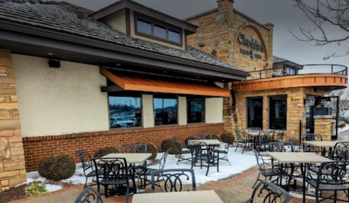 Exterior of a restaurant with stone accents, outdoor seating, and snow on the ground.