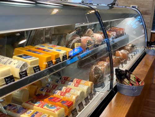 A display case filled with various cheeses and cured meats, neatly arranged with labels on each item.