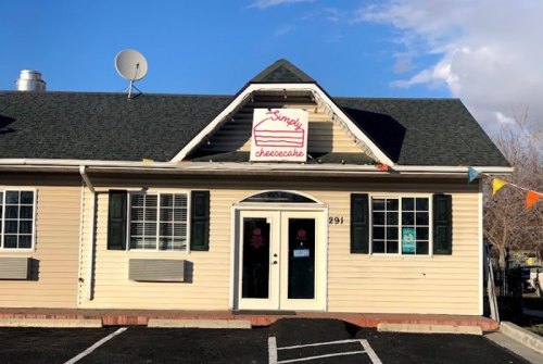 Exterior of a cream-colored building with a sign reading "Sandy's Cheesecake," featuring green shutters and a satellite dish.