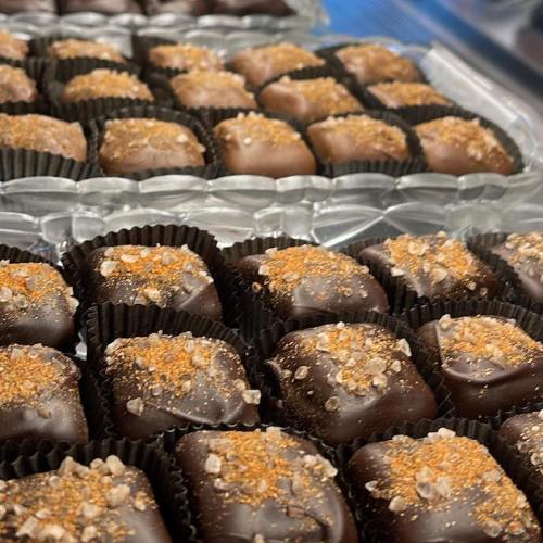 A close-up of assorted chocolate confections topped with crushed nuts and spices, arranged in black paper cups.