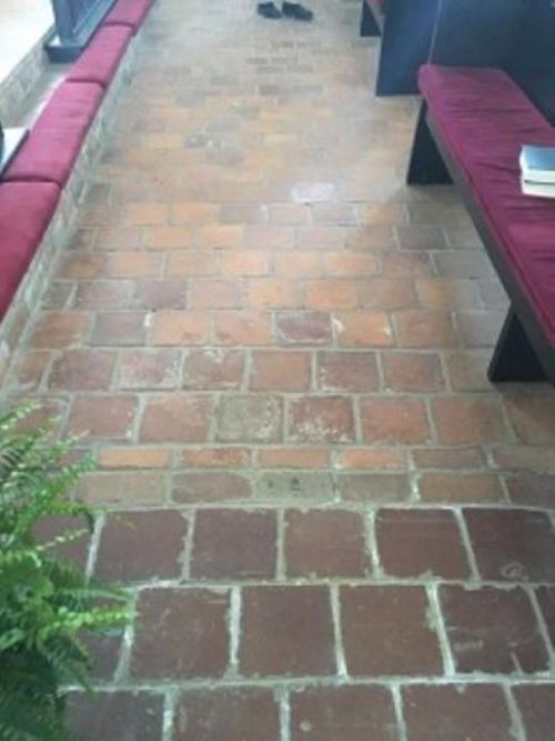 A view of a brick floor in a hallway, with benches on either side and a few books resting on a table.