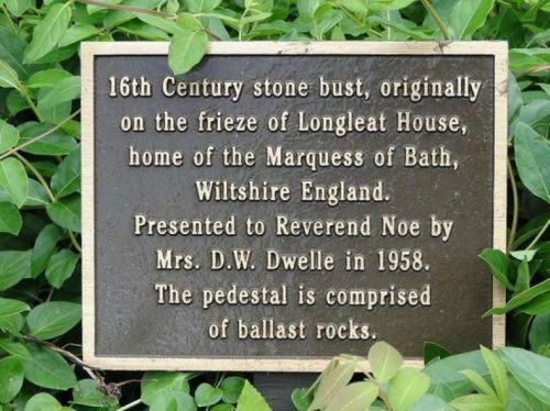 Plaque detailing a 16th-century stone bust from Longleat House, presented to Reverend Noe in 1958, on a rocky pedestal.