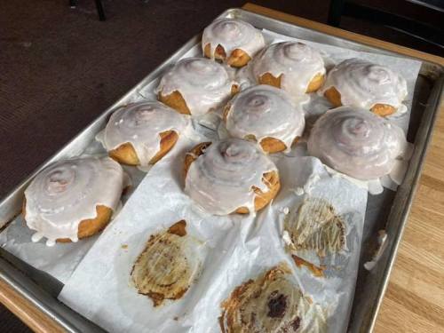 A tray of freshly baked cinnamon rolls topped with white icing, some partially eaten, on parchment paper.