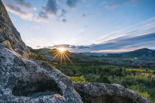 A stunning sunset over a mountainous landscape, with rays of sunlight shining through clouds and rocky foreground.