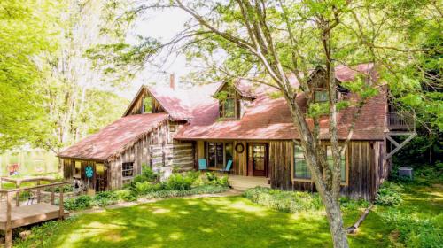 A charming wooden cabin surrounded by lush greenery and trees, featuring a welcoming porch and a sloped roof.