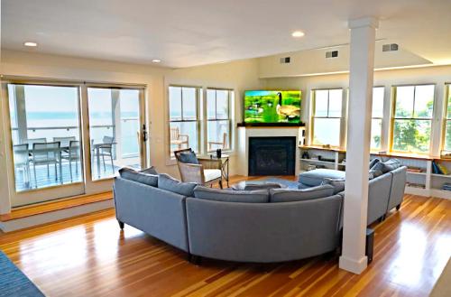 Bright living room with a large sectional sofa, TV, and views of the ocean through large windows. Hardwood floors shine.