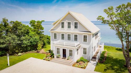 A beautiful white house by the water, surrounded by greenery and featuring a spacious front porch.