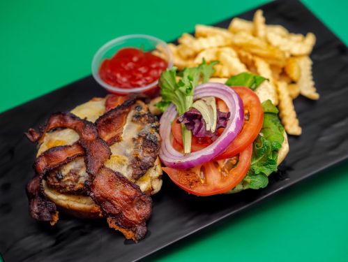 A bacon cheeseburger with fresh vegetables, served with crinkle-cut fries and a side of ketchup on a black plate.
