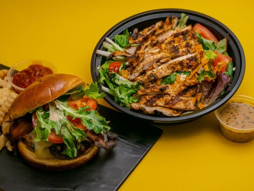 A delicious burger with lettuce, tomato, and cheese, alongside a grilled chicken salad and a side of beans.