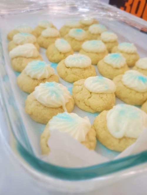 A tray of freshly baked cookies topped with white frosting and blue accents, arranged neatly in a glass dish.