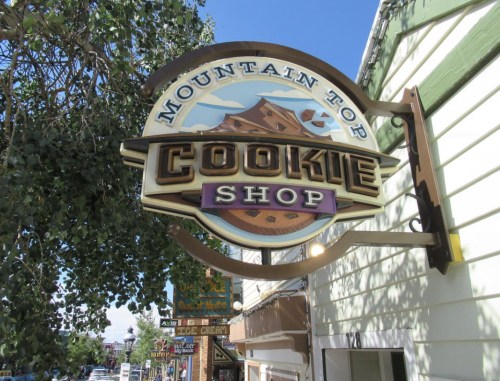 Sign for "Mountain Top Cookie Shop" hanging from a building, with a clear blue sky in the background.