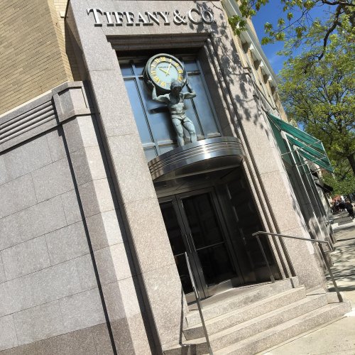 Exterior of a Tiffany & Co. store featuring a clock and a statue above the entrance, surrounded by trees.