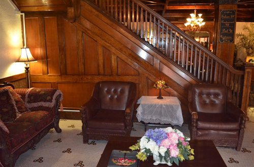 Cozy interior with wooden staircase, two leather armchairs, a floral centerpiece, and warm lighting.