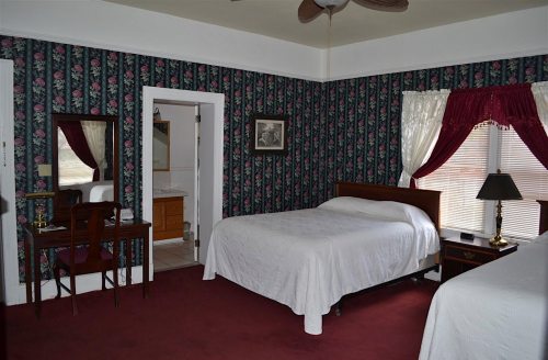 A cozy bedroom with floral wallpaper, two beds, a desk, and an adjoining bathroom.