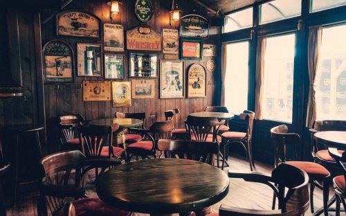 Cozy pub interior with wooden walls, vintage signs, and empty tables and chairs bathed in natural light.