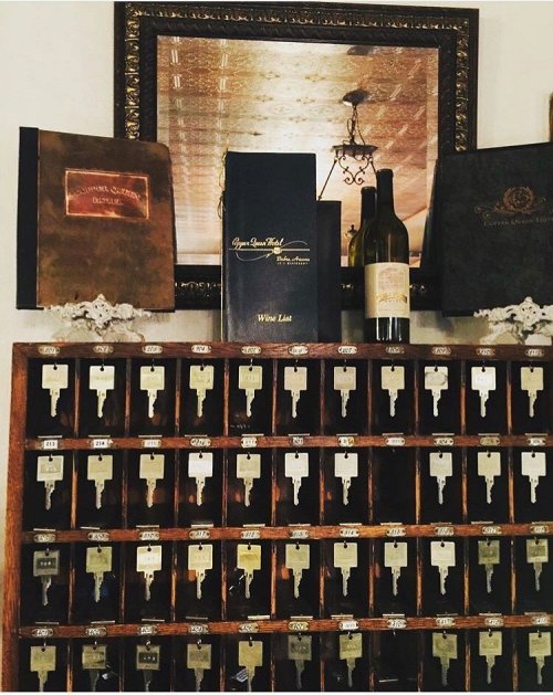 A vintage key holder with numerous keys, a wine bottle, and a wine list displayed above in an elegant setting.