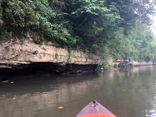 A view from a kayak on a calm river, with rocky cliffs and lush greenery lining the banks.